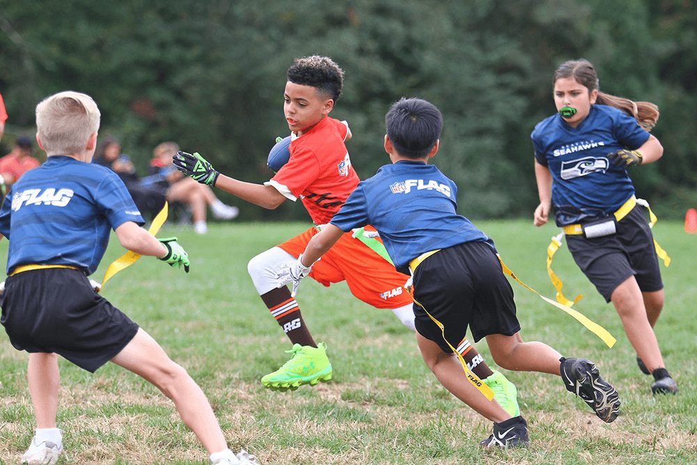 Players in blue chase a ball carrier in orange during a flag game