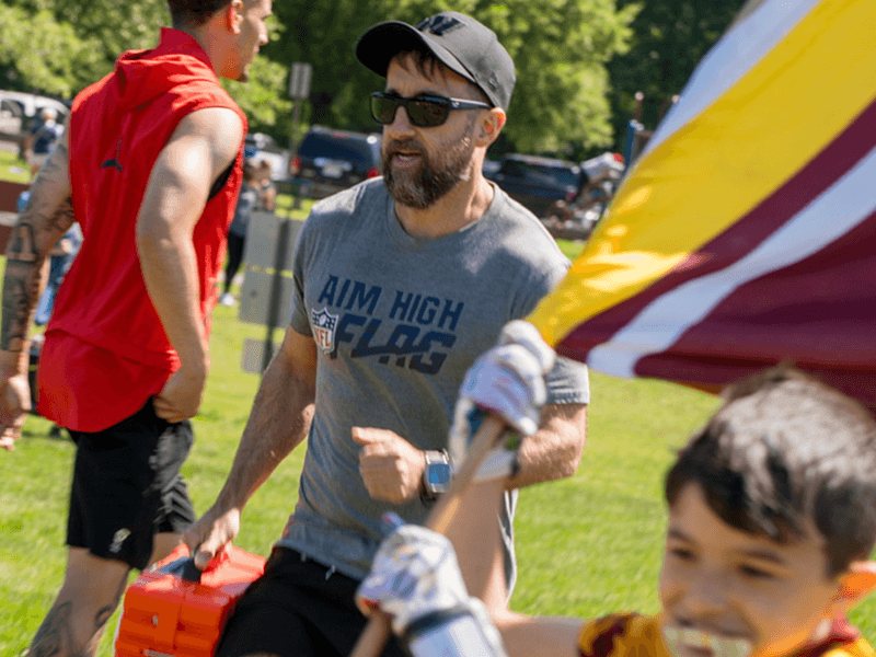 Coach Joe DePalma in an Aim High Flag tee runs alongside players on game day